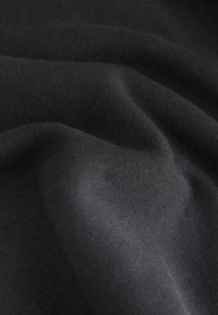 Schwarzer, weicher Stoff mit glatter Textur, der leichte Falten und Knicke zeigt. Das Material wirkt leicht und vielseitig einsetzbar.