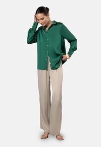 Green satin button-up shirt with a collar, paired with beige wide-leg trousers. Features a relaxed fit and button details on sleeves.