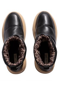 Botas negras de piel sin cordones con suelas marrones y forro de tela de estampado de leopardo, vistas desde arriba sobre un fondo blanco.