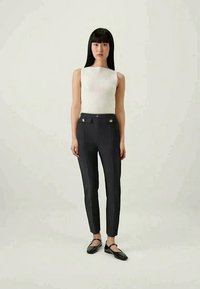 Bijela rebrasta majica bez rukava u kombinaciji sa uskim tamnosivim hlačama sa zlatnim dugmadima i crnim balerinkama. Glatka tekstura i kroj po meri.