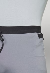 Shorts de bain gris avec une taille élastique noire, un cordon de serrage et un accent logo texturé noir sur le côté.