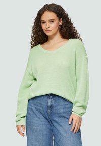 Mintgrüner, übergroßer Strickpullover mit V-Ausschnitt, strukturiertem Stoff und langen Ärmeln, kombiniert mit hoch taillierten blauen Jeans.