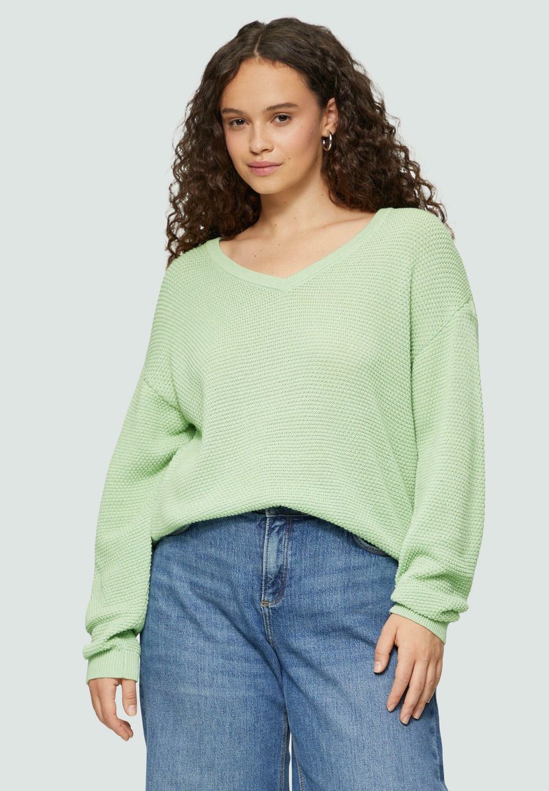 Mintgrüner, übergroßer Strickpullover mit V-Ausschnitt, strukturiertem Stoff und langen Ärmeln, kombiniert mit hoch taillierten blauen Jeans.