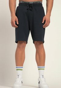 Marineblaue Sportshorts mit einem Kordelzugbund und einem elastischen Band mit Markenlogo. Kombiniert mit weißen Sneakers und mehrfarbigen Crew-Socken.