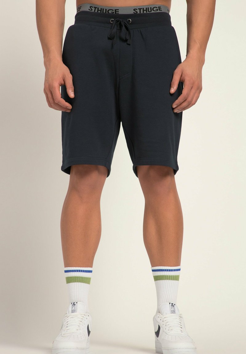 Marineblaue Sportshorts mit einem Kordelzugbund und einem elastischen Band mit Markenlogo. Kombiniert mit weißen Sneakers und mehrfarbigen Crew-Socken.