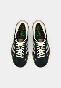 Adidași din piele întoarsă neagră cu trei dungi albe, cu modele florale pe partea din față, talpă texturată și branț floral colorat.