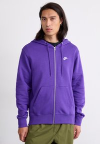 Sweatshirt roxo com fecho éclair, feito de uma mistura de algodão, com bolsos frontais, cordões e um logo branco da Nike no lado esquerdo do peito.