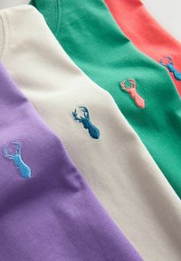 Vier T-Shirts gestapelt, gezeigt in den Farben Lila, Creme, Grün und Koralle. Jedes hat ein kleines, besticktes Hummerdesign in verschiedenen Blau- und Rosatönen.