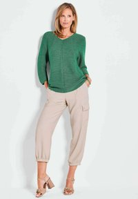 Groene geribbelde trui met V-hals, gedragen met beige cargobroek met zijzakken en bruine sandalen met hak en banddetail.