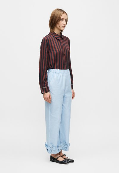 Cămașă cu mâneci lungi în dungi negre și roșii, pantaloni bleu deschis cu șiret și aplicații florale la manșete, asortați cu balerini negri.