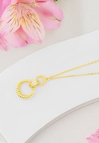 Guldhalsband med sammanflätade cirkulära hängen; en med textur, den andra slät med små glittrande stenar, på en fin kedja.