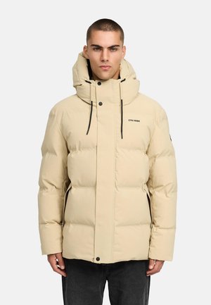 Beige puffer jacket with a high collar and drawstring hood. Featuring a front zipper and snap buttons, it has a quilted design and black accents.
