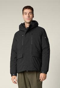 Giacca nera isolata con cappuccio, dotata di due tasche sul petto con zip e grandi tasche frontali, realizzata in materiale liscio e resistente alle intemperie.