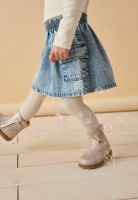 Jeansrock mit elastischem Bund und einer Gesäßtasche, kombiniert mit beigen Stiefeletten und hellen Strickstrumpfhosen, im Hintergrund Blasen.