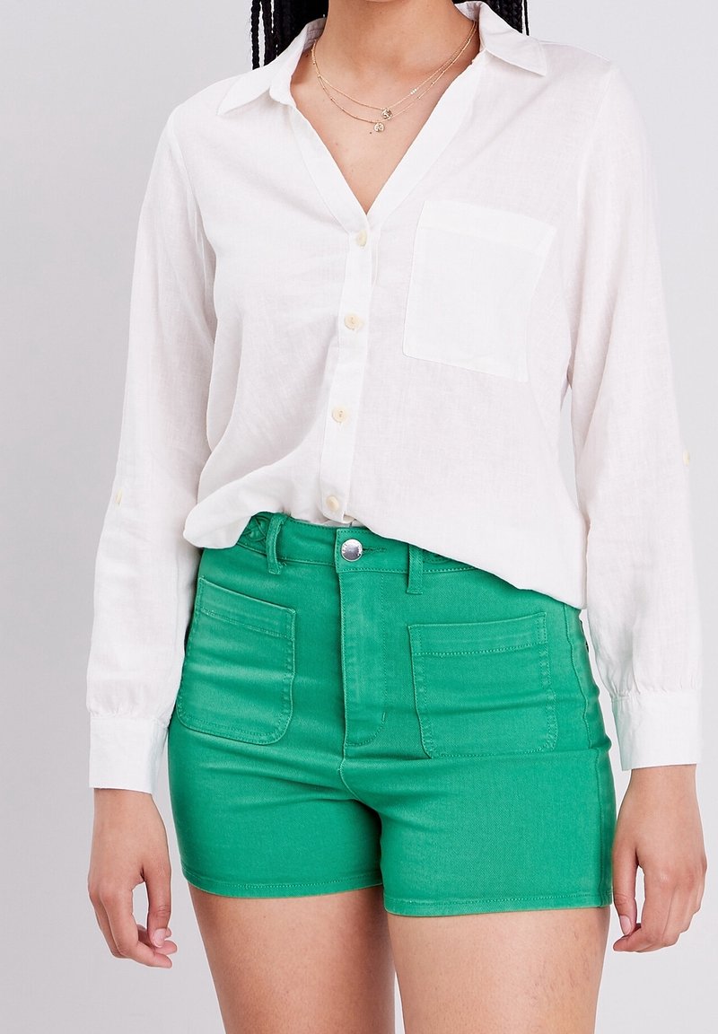 Chemise blanche à manches longues avec poches sur la poitrine, associée à un short en denim vert taille haute avec poches avant et fermeture à bouton.