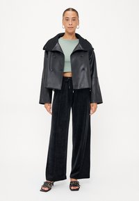 Svart skinnjakke med dobbel knapping og bred krage, parret med løse svarte fløyelsbukser og svarte sandaletter med stropper. Grønn crop top under.