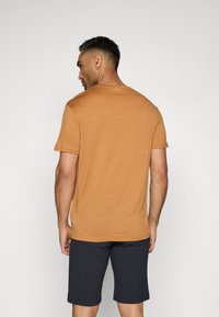 Kortermet t-skjorte med rund hals i okerfarge, laget av myk stoff, brukt med mørke shorts. Utsikt fra baksiden, som viser en avslappet passform.