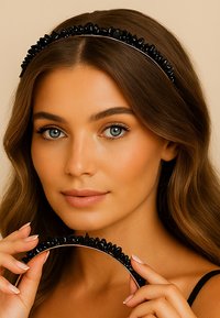 Czarna opaska na głowę z błyszczącymi kamieniami wzdłuż górnej krawędzi, o gładkim, zakrzywionym kształcie, trzymana przez osobę z długimi, falującymi włosami.