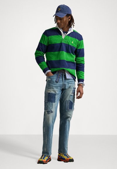 Green and navy striped rugby shirt, blue patched denim jeans, and colorful sneakers. Features a baseball cap and layered collar.