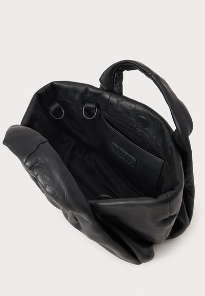 Sac cabas en cuir noir souple avec poignées rembourrées, ouverture sur le dessus, poche intérieure et deux anneaux métalliques à l'intérieur.