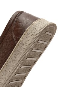Sneaker in pelle marrone con una superficie textured, dotato di una suola in gomma beige e linee di trazione orizzontali per una migliore aderenza.