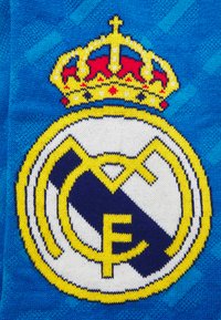 Pletená tkanina s logom Real Madrid. Dizajn zahŕňa zlatú korunu, modro-bielu farebnú schému a detailné prešitie emblému.