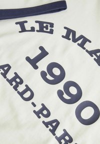 Witte stoffen t-shirt met een marineblauwe grafische print waarop "LE MARAIS 1990" in gebogen tekst staat, met een geribbelde marineblauwe kraag.