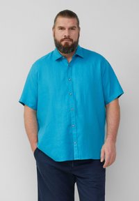 Kortebladige, knoopshirt in fel turquoise linnenstof. Heeft een klassieke kraag en een subtiele glans, gecombineerd met donkere broeken.