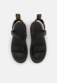 Black sandals with adjustable Velcro straps, a textured upper, and a cushioned sole. Features a yellow pull tab at the back.