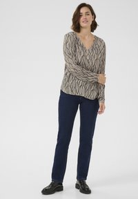 Long-sleeve, V-neck blouse featuring a beige and navy wave pattern. Paired with dark blue jeans and black chunky shoes.