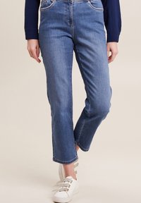 Lichtblauwe denim jeans met een rechte snit, ge.cropte zoom en subtiele vervaging. Gecombineerd met witte sneakers met decoratieve veters.