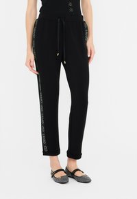 Zwarte joggingsbroek met een comfortabele tailleband en trekkoord, voorzien van een glanzende logostrijp langs de zijkanten en opgerolde manchetten.