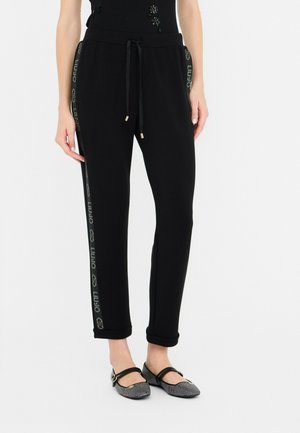 Pantalons de jogging noirs avec une taille confortable et un cordon de serrage, présentant une bande à logo brillant sur les côtés et des ourlets retroussés.