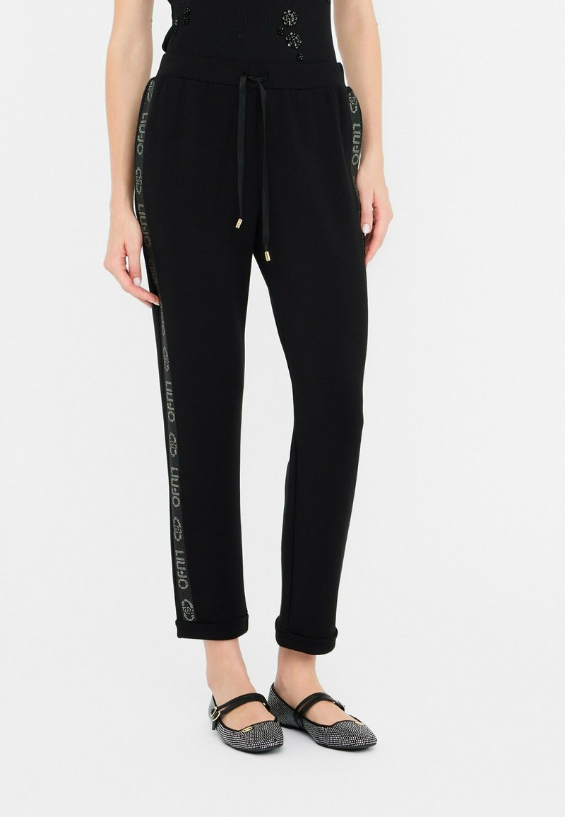 Zwarte joggingsbroek met een comfortabele tailleband en trekkoord, voorzien van een glanzende logostrijp langs de zijkanten en opgerolde manchetten.