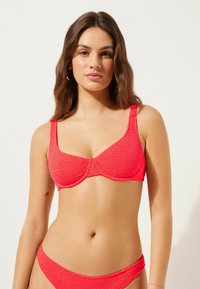 Roter Textur-Bikini-Oberteil mit breiten Trägern und Unterdrahtformung. Der Stoff weist ein dezentes Zickzackmuster auf, das ein komplexes visuelles Detail bietet.