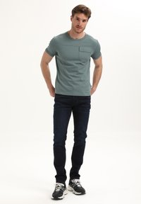 Svetle zelené tričko s krátkým rukávem a náprsní kapsou, spárováné s tmavě modrými skinny džíny a černými sportovními botami s bílými detaily.