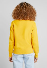 Pullover in cotone giallo brillante con orlo e polsini a costine, caratterizzato da un design semplice e una vestibilità rilassata. Dettagli di cucitura visibili.