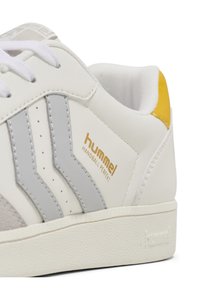 White athletic shoe with grey and yellow accents, featuring a textured sole, smooth synthetic upper, and gold branding on the side.