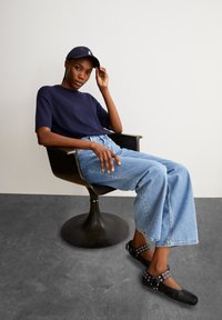 Marineblauw geribbelde top met korte mouwen, gecombineerd met lichtblauwe hoge taille wijde jeans en zwarte flats met ronde accenten, zittend in een zwarte stoel.