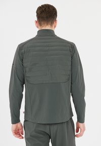 Grå jacka med en slät yta och kviltad bakpanel, med ståkrage och långa ärmar, tillverkad av ett lätt tyg.