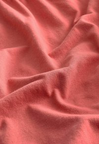 Korallfärgad tyg med en mjuk, texturerad yta, med subtila nyansvariationer och ett lent, flödande fall mot en veckad bakgrund.