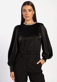 Zwarte satijnen top met pofmouwen en een metallic rand bij de hals, gecombineerd met zwarte, op maat gemaakte broek met een slanke pasvorm en een gladde textuur.
