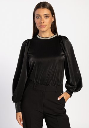 Zwarte satijnen top met pofmouwen en een metallic rand bij de hals, gecombineerd met zwarte, op maat gemaakte broek met een slanke pasvorm en een gladde textuur.
