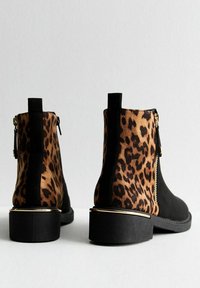 Pár černých kotníkových bot s leopardím vzorem na zadních panelech, zlatým zipem a blokovými podpatky se zlatým lemem, zobrazených ze zadního a bočního úhlu.