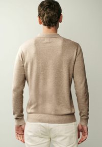 Beigen värinen ohut neulepaita, jossa on pitkät hihat, istuvat hihansuut ja resorireuna. Selkeä muotoilu ilman näkyviä kuvioita tai metalliosia.