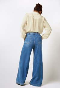Cream blouse with puff sleeves, paired with high-waisted, wide-leg blue denim jeans featuring two back pockets and visible stitching.