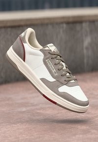 White and grey athletic sneaker with a textured upper, lace closure, red accents on the sole, and a logo on the tongue.