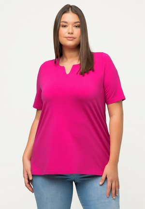 Top fucsia a maniche corte con scollatura a V. Tessuto morbido e leggero che si adagia liberamente sul corpo, abbinato a jeans in denim chiaro.