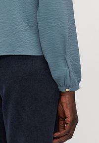 Lichtblauw shirt van textuurstof, met lange mouwen en knoopmanchetten, in combinatie met donkerblauwe corduroy broek.