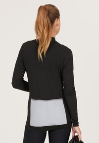 Svart långärmad sporttröja med en grå bakpanel som har "ENDURANCE"-logotypen. Materialet verkar jämnt och elastiskt.